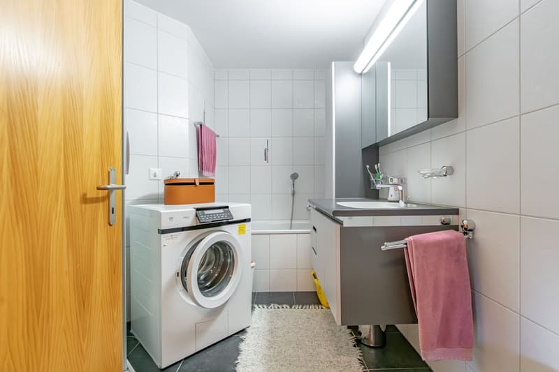 white washer, sink, small white tile flooring, bathtub, tiled walls, pink towels
