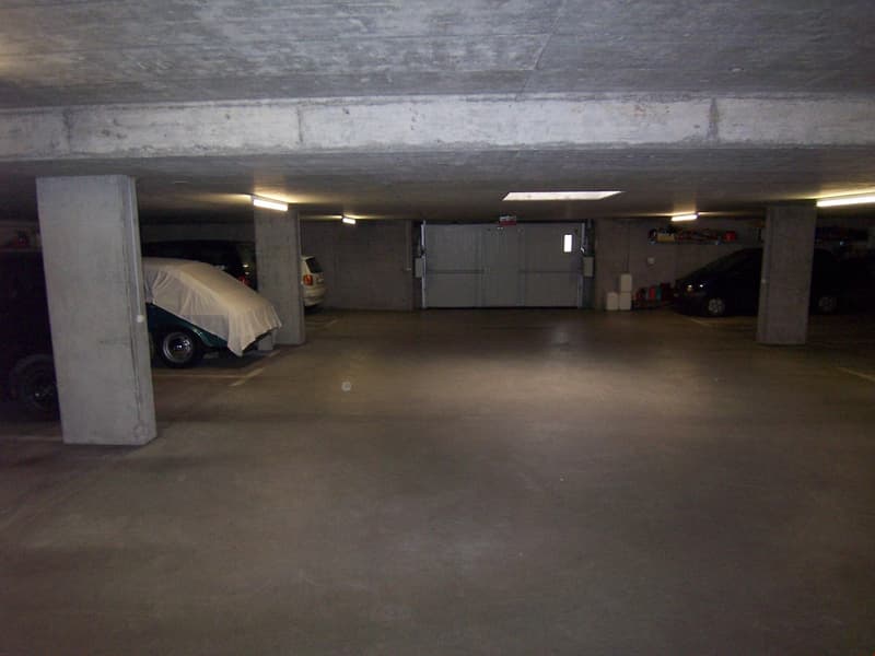 Underground parking garage with concrete walls and floor, covered vehicle, and storage space