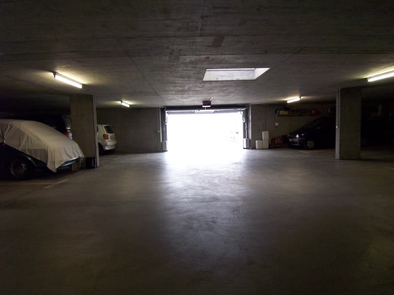Large open garage space with concrete floor, overhead lighting, and a covered vehicle parked inside.