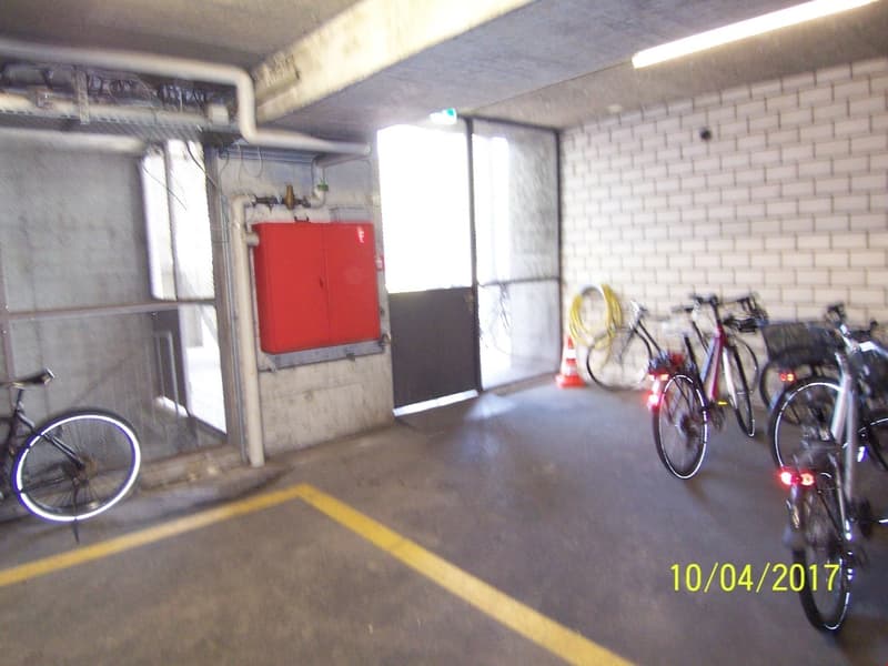 The image shows a garage space with a red storage cabinet, several bicycles parked, and a concrete floor with yellow markings.