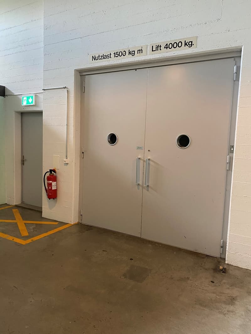 The image shows a large industrial door with a sign indicating a maximum load capacity of 1500 kg/m2 and a lift capacity of 4000 kg. The door appears to be part of a warehouse or industrial facility.