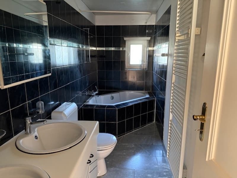 Bathroom with black tiles, bathtub, toilet, sink, mirror, and window