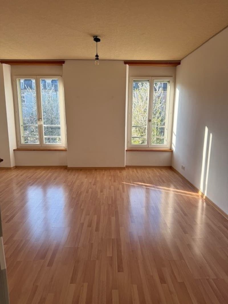 Empty room with wooden floor, two windows, white walls, and a ceiling light