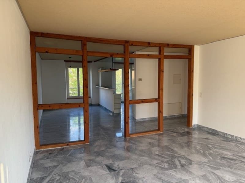 Empty room with wooden doors, white walls, gray floor, windows, and a ceiling light.