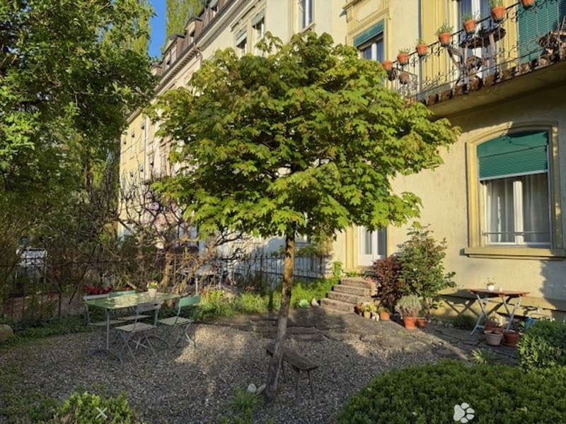 A garden with a table and chairs, a tree, plants, and a building with a balcony and windows