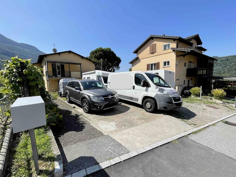 Two houses, brick houses, 2 cars and 2 vans parked in front, grassy area, driveway, mailbox, clear blue sky