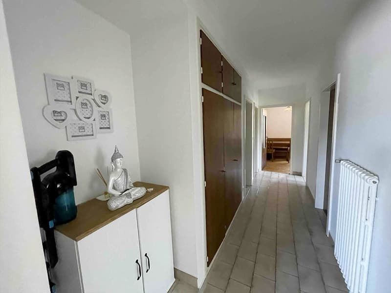 white walls, tiled floor, white cabinet with brown top, brown doors, framed pictures, radiator, statue, blue jug, and black object