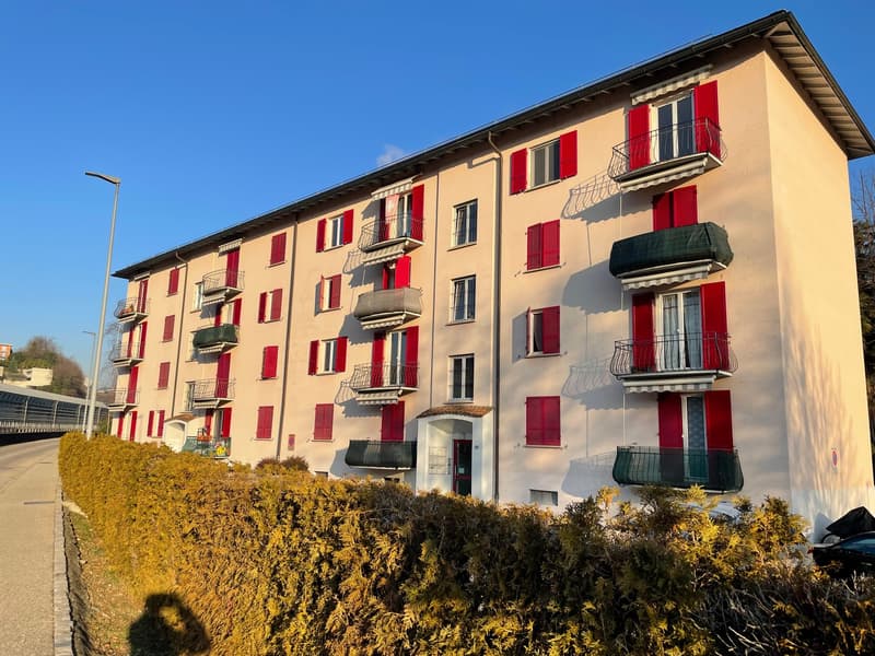 4 story apartment building, beige, red shutters, multiple balconies, hedges in front