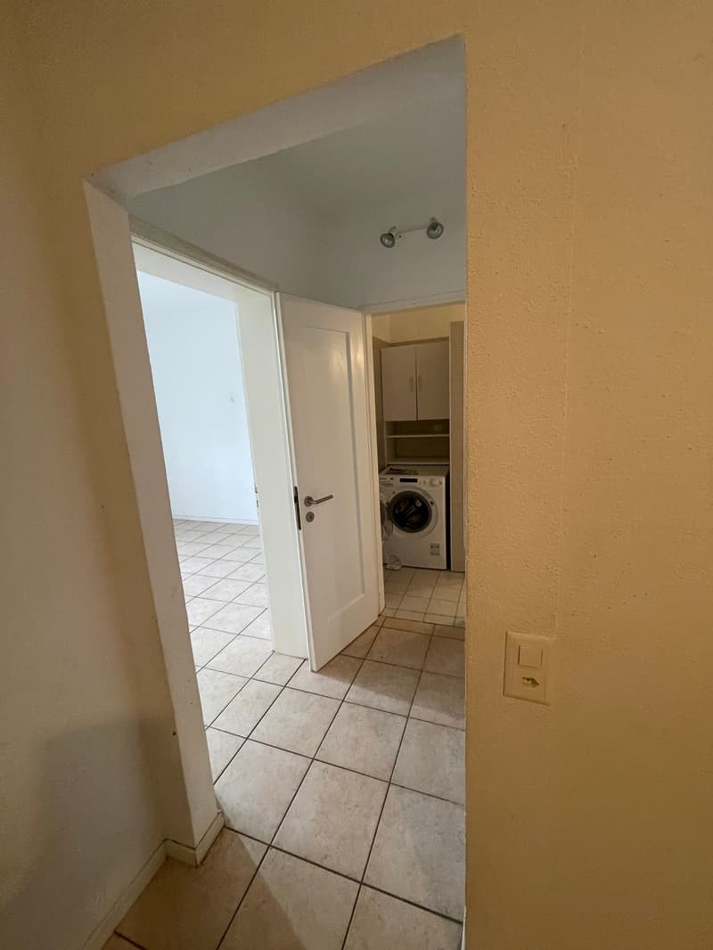 Room with hallway, door, washing machine, tiled floor, shelves, lights.