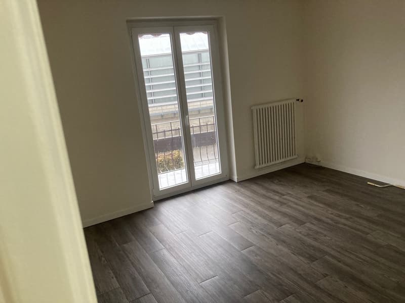 Empty room with glass doors, white walls, wooden floors, white radiator