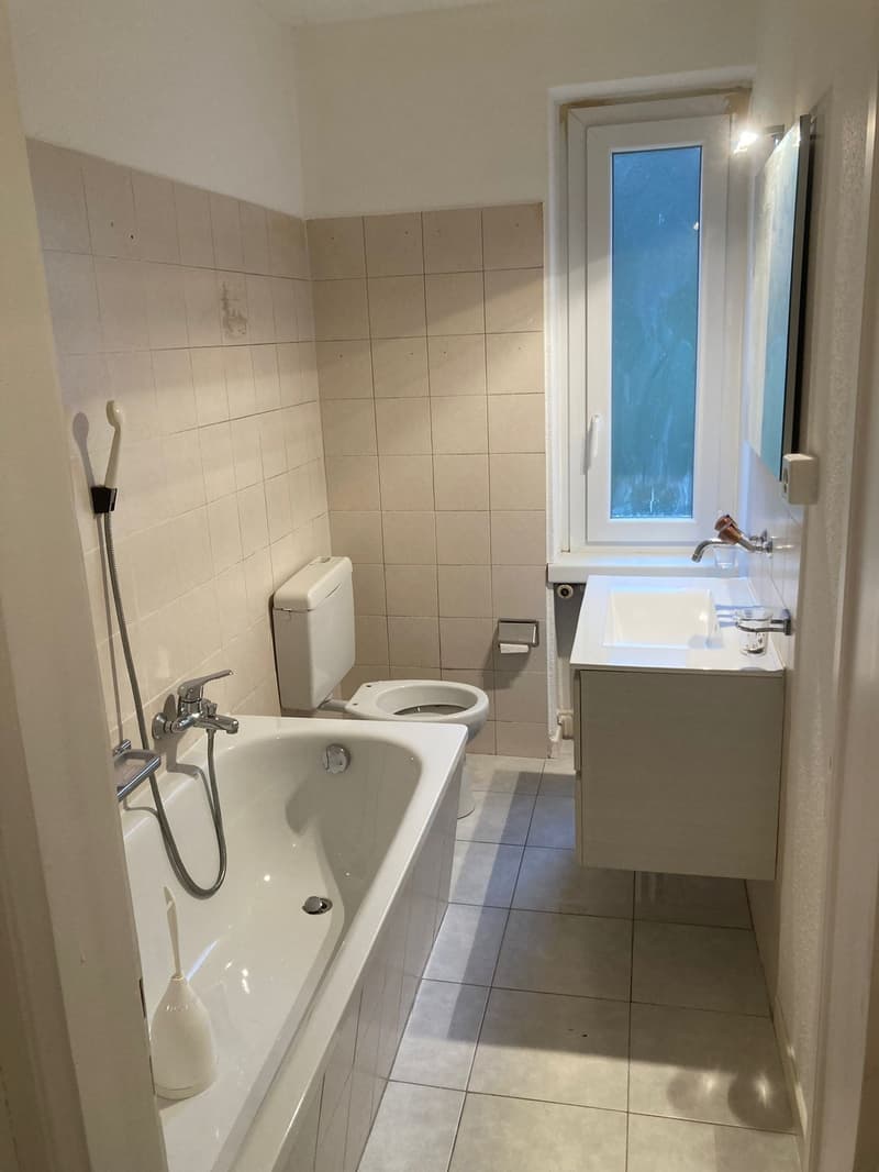Bathroom with bathtub, toilet, sink, and mirror.