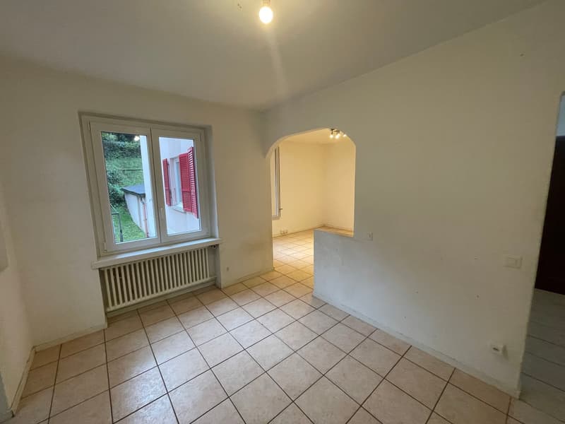 Empty room with white walls, tiled floor, window with shutters, and a small radiator below the window