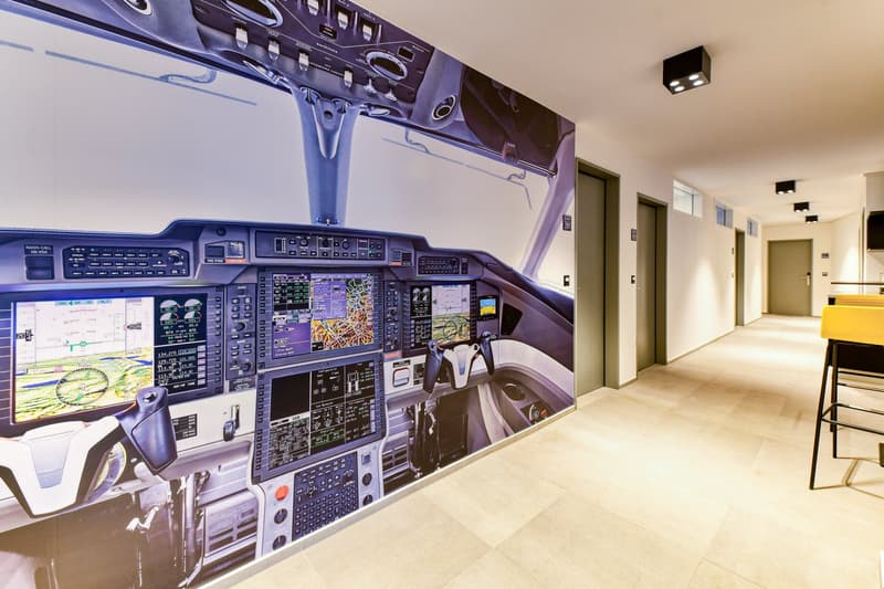Long corridor with airplane cockpit mural, beige tiles, wooden bar stools