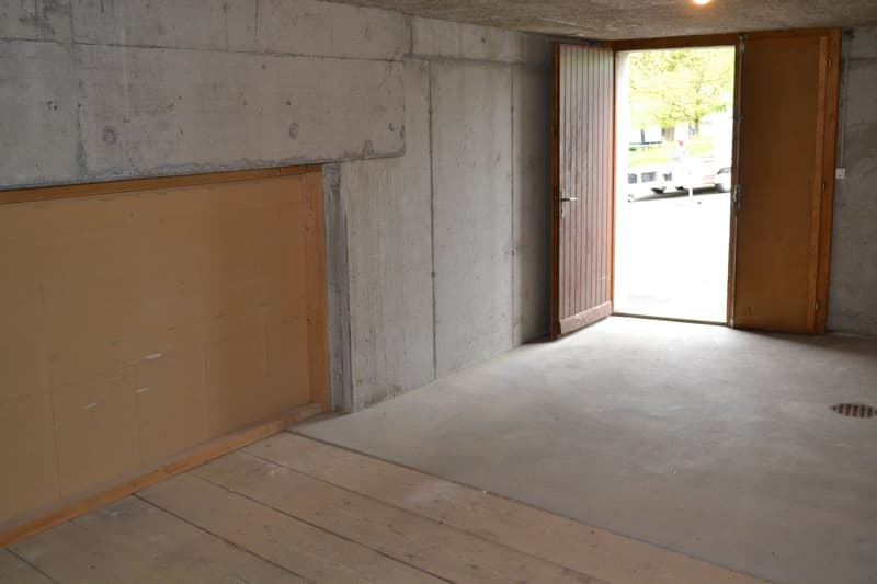 Unfinished concrete walls, wooden floor, open doorway leading to the outside