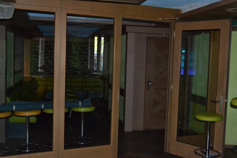 This image shows an interior space with large windows, a wooden door, and bar stools in front of the windows. The room has a modern, minimalist design with neutral colors and clean lines.