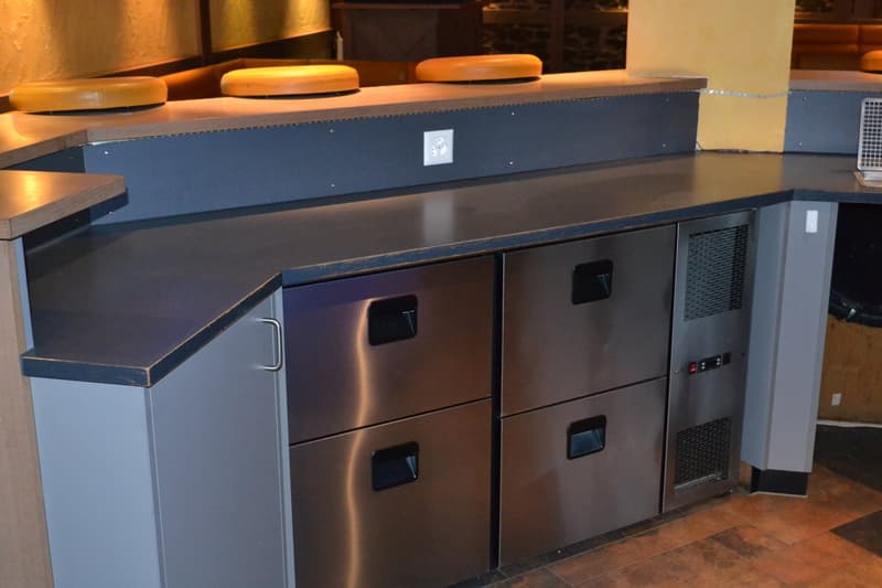 Commercial-grade kitchen equipment, including a stainless steel dishwasher and refrigerator units, with a dark countertop surface.