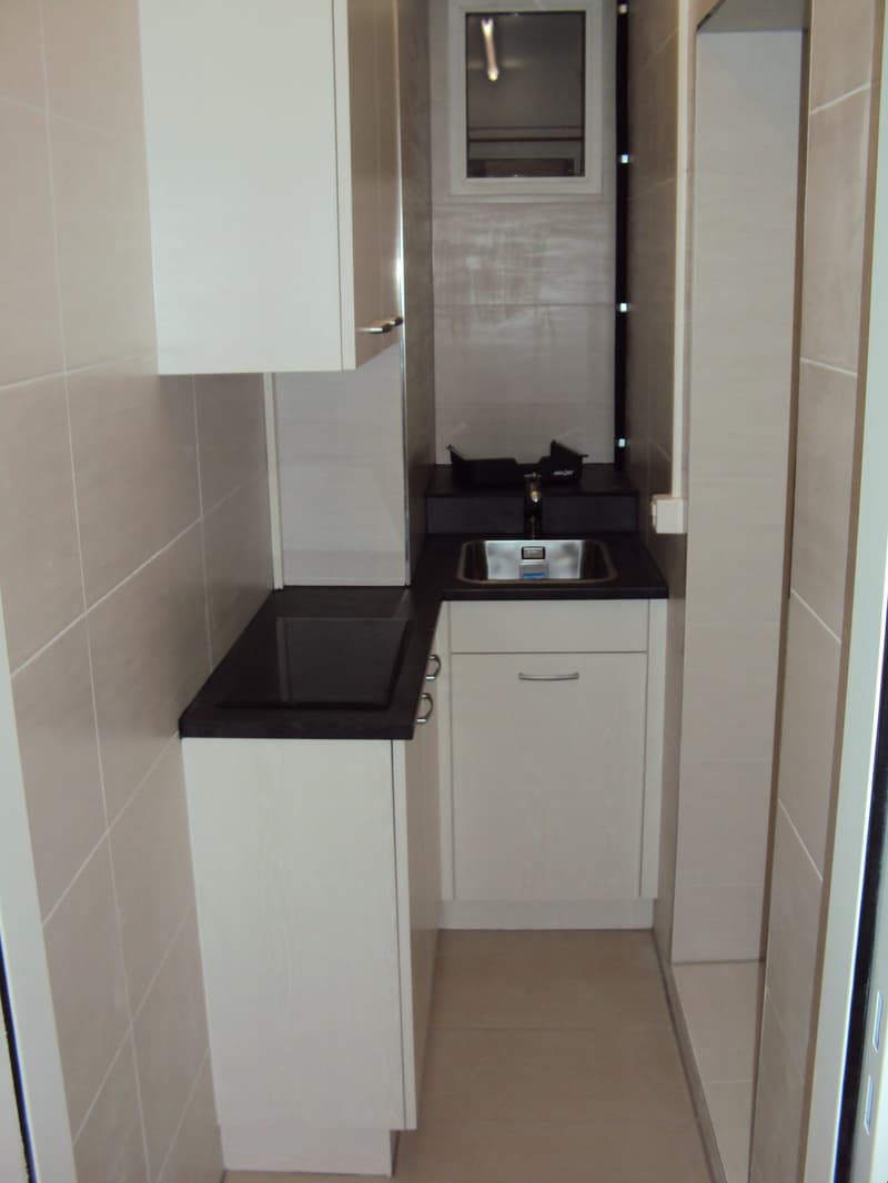 Small kitchen with white cabinets, black countertop, sink with faucet, dishwasher and washing machine.