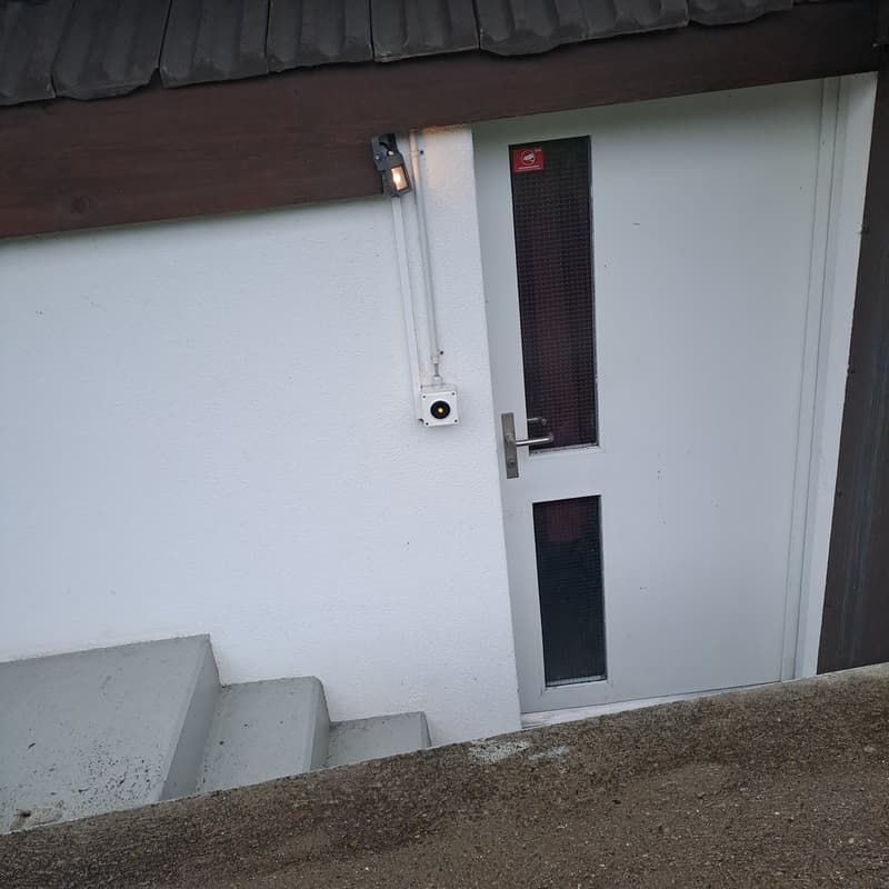 White exterior wall, white door, surveillance camera, light fixture, stairs leading up to the door