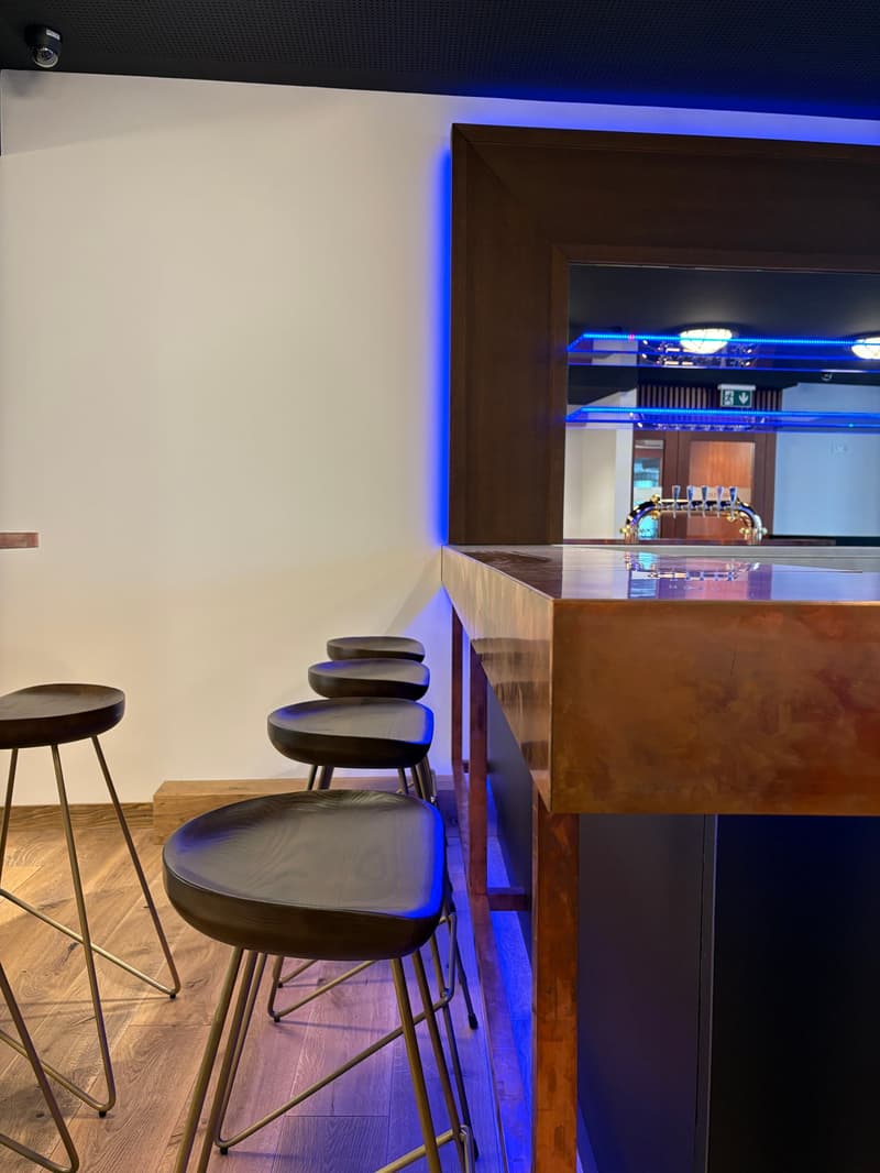 Bar counter with stools, wooden flooring, white wall, blue lights