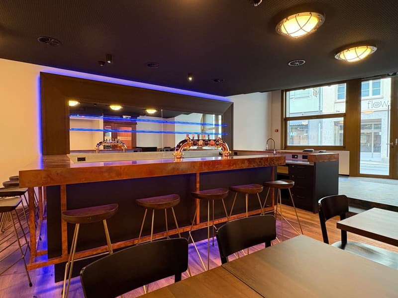 wooden flooring, open layout, metal and wooden bar stools, bar counter, illuminated blue shelves, large windows