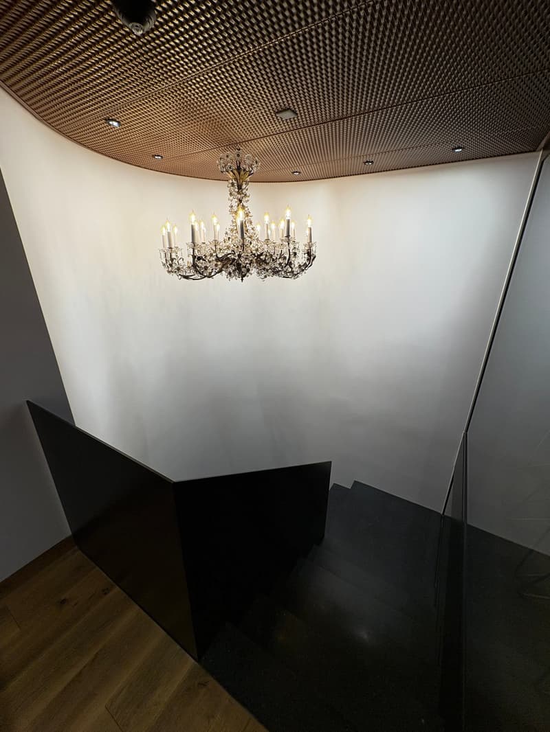 Chandelier in middle of room, wooden floors, modern staircase, glass wall