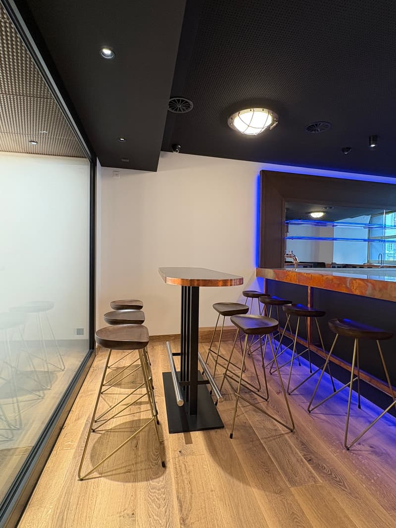 a small bar area with a central table, metal stools, wood flooring, a bar counter, and glass walls