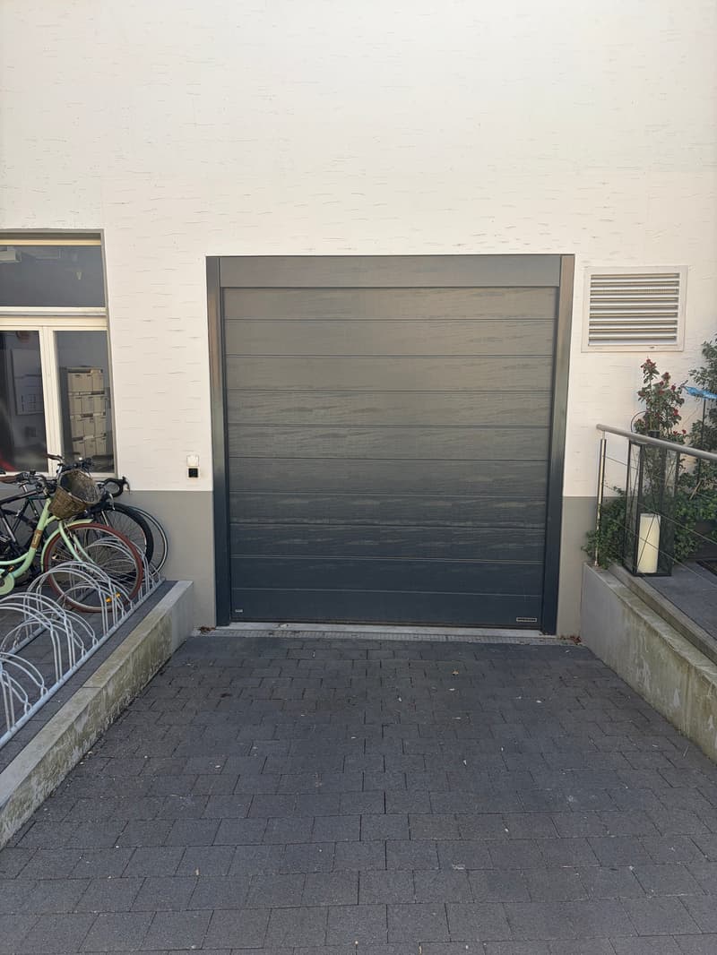 A large black garage door with a metal railing on the right side, a white wall on the left side, and a bicycle rack on the left side.