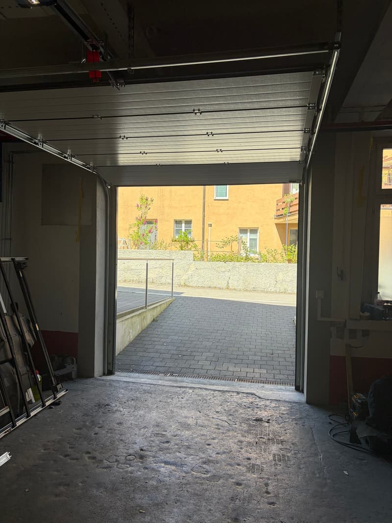 Empty garage with a brick floor, metal ceiling, and an open door leading to a paved walkway.