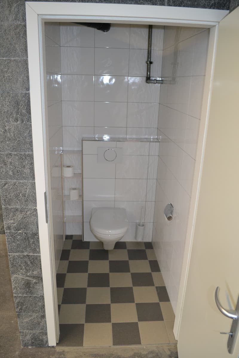 small bathroom with toilet, tiled walls, checkered floor, toilet paper holder, toilet brush