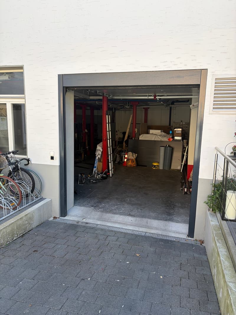 Open garage with bicycles parked outside, storage boxes, ladders, and various tools inside