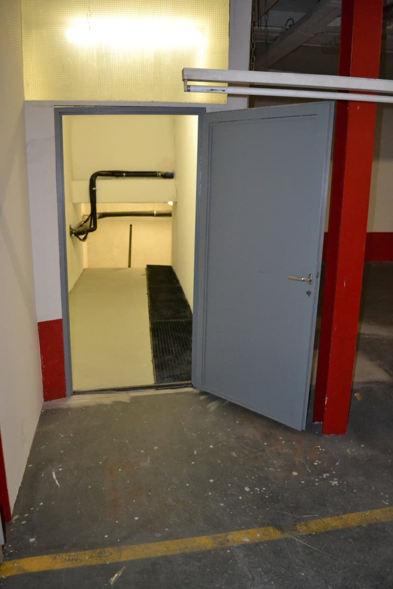 garage entrance, open door, concrete floor, metal grate, pipes