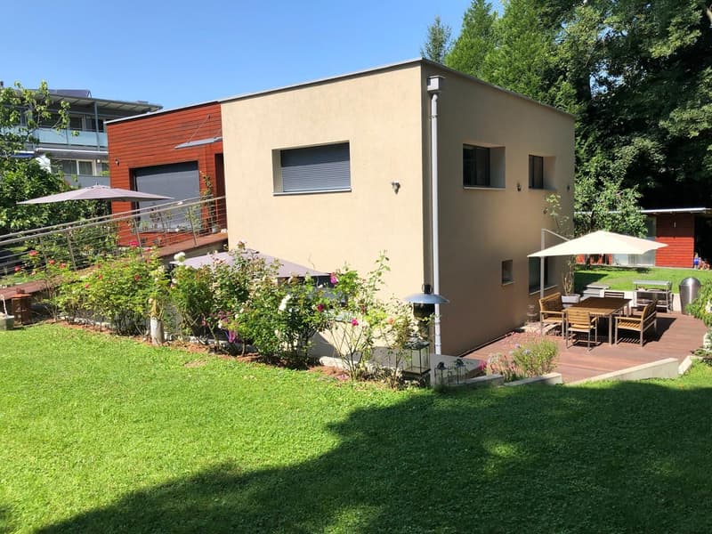 Modern house with beige and red walls, wooden deck, outdoor dining area, garden, trees, and plants