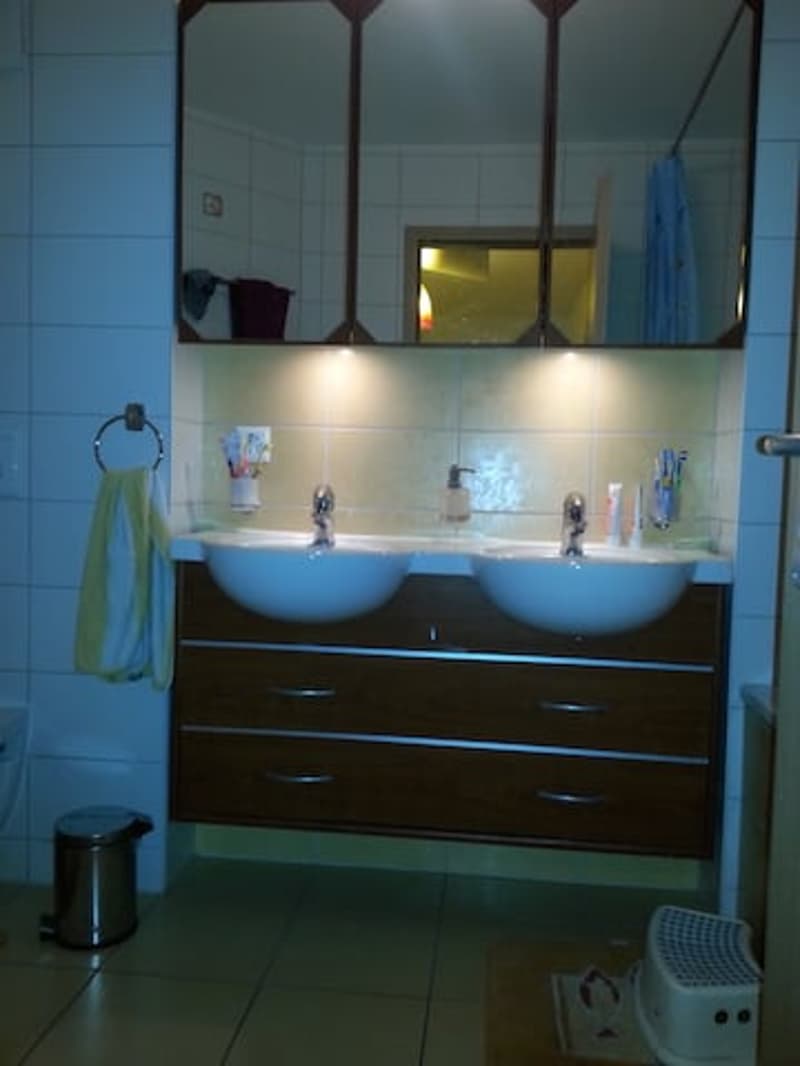 Bathroom with two sinks, wooden cabinet, mirror, tiled floor, trash can, and towel rack