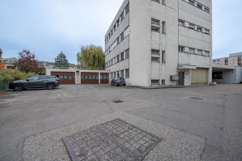 Large building with multiple windows, garage doors, and a car park area.