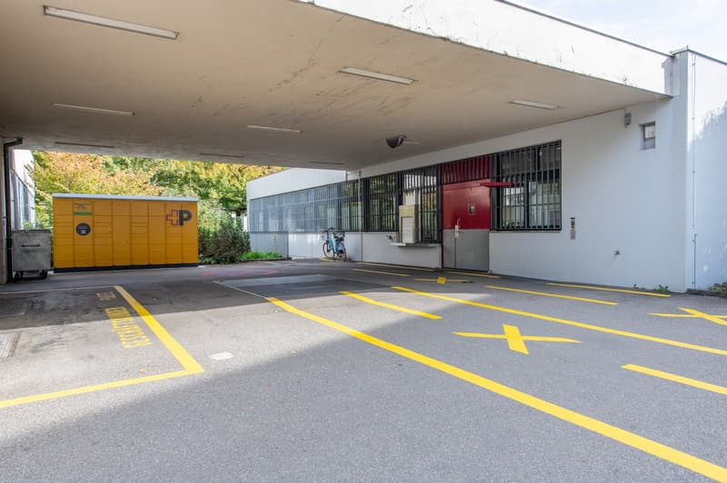 White building with multiple windows, an orange storage unit, a parked bicycle, yellow markings on the road