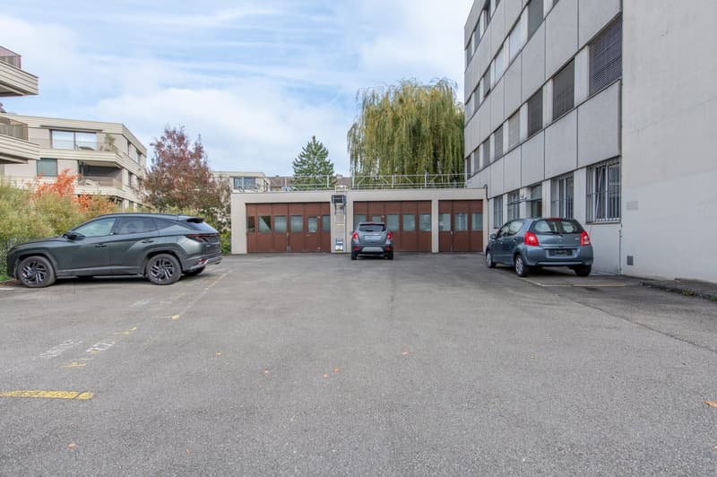 parking lot with three cars parked, a building with garage doors on the left, another building with windows on the right