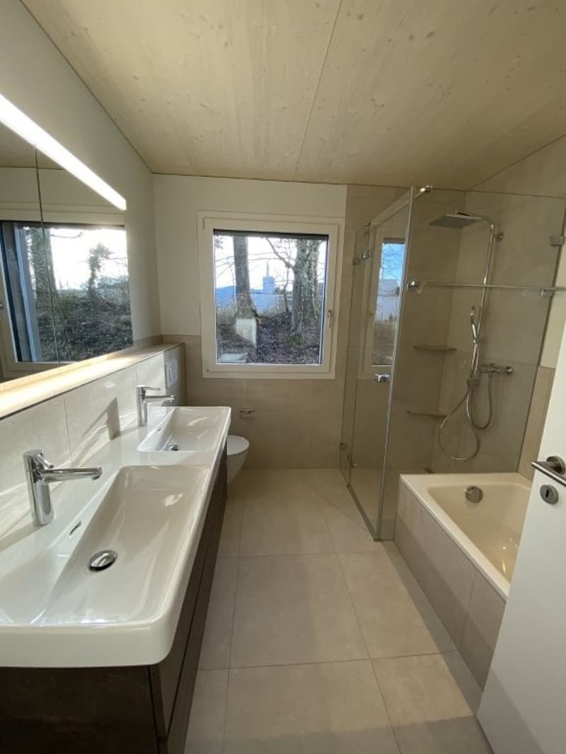 Spacious bathroom with large window providing a view, double vanity sink, bathtub, and walk-in shower