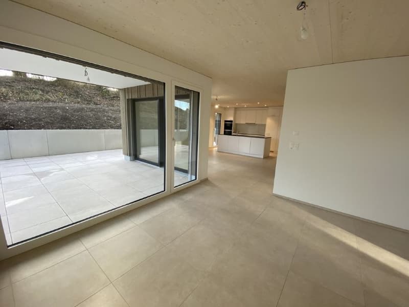 Spacious open-plan living area with large sliding glass doors leading to a balcony or terrace, hardwood floors, and a modern kitchen visible in the background.