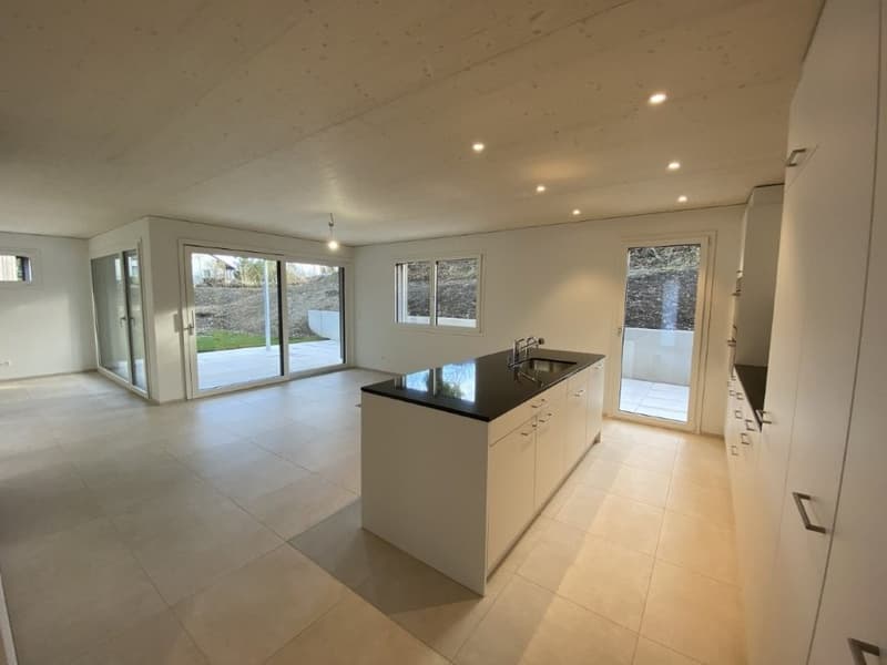 Spacious open-plan living area with large windows, modern kitchen with black countertop, and sliding glass doors leading to a balcony or terrace.