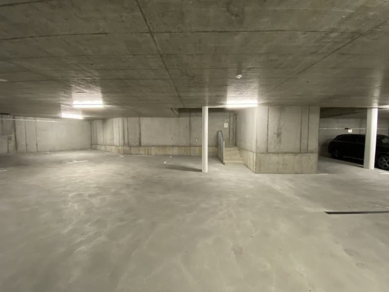 Large open concrete parking garage with multiple levels, concrete walls and floors, and overhead lighting.