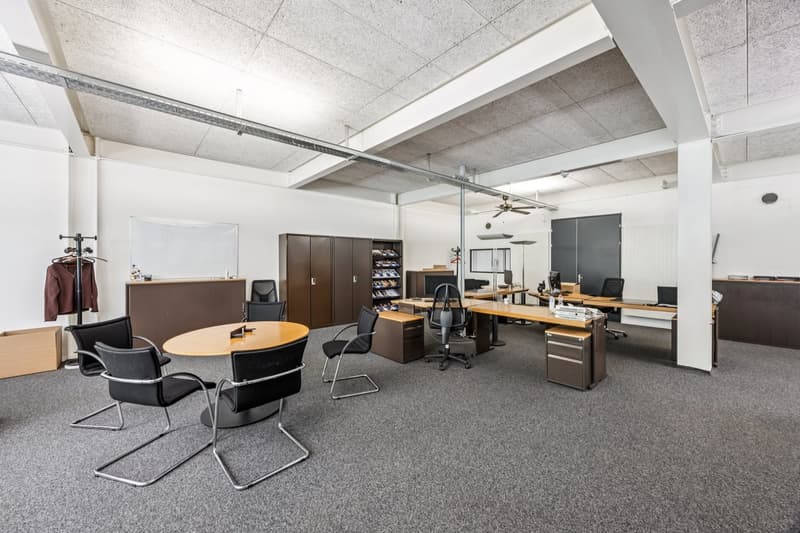 Large open office space with concrete ceiling, desks, chairs, storage cabinets, and a dishwasher visible