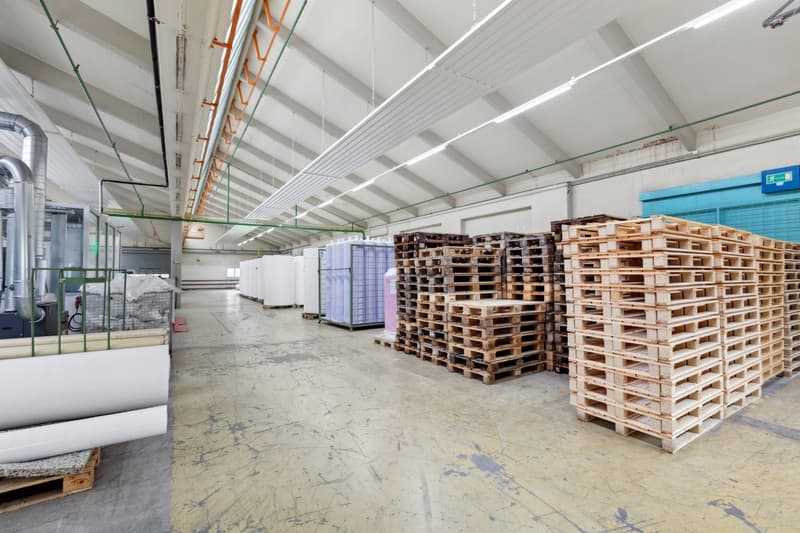 Large industrial warehouse space with high ceilings, stacks of wooden pallets, and various equipment and storage containers.