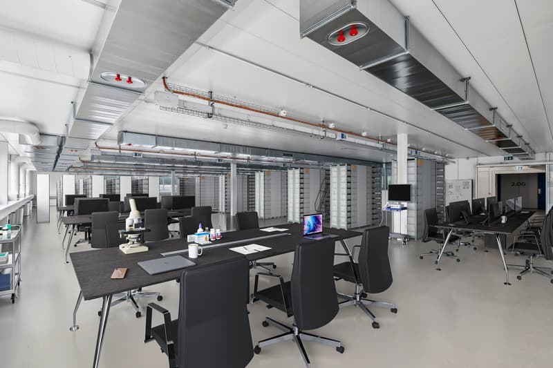 Large open office space with multiple workstations, black chairs and desks, computer monitors, and overhead lighting fixtures