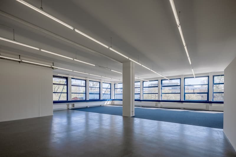 an empty room with multiple large windows, concrete floor, white walls