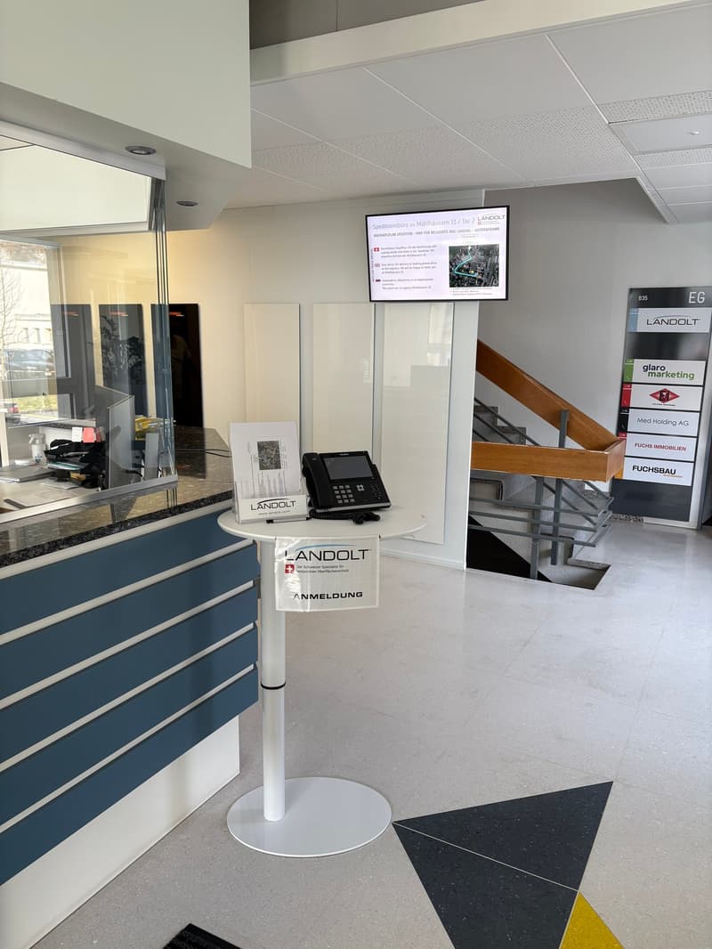 Lobby area with desk, telephone, monitor, posters, and a staircase
