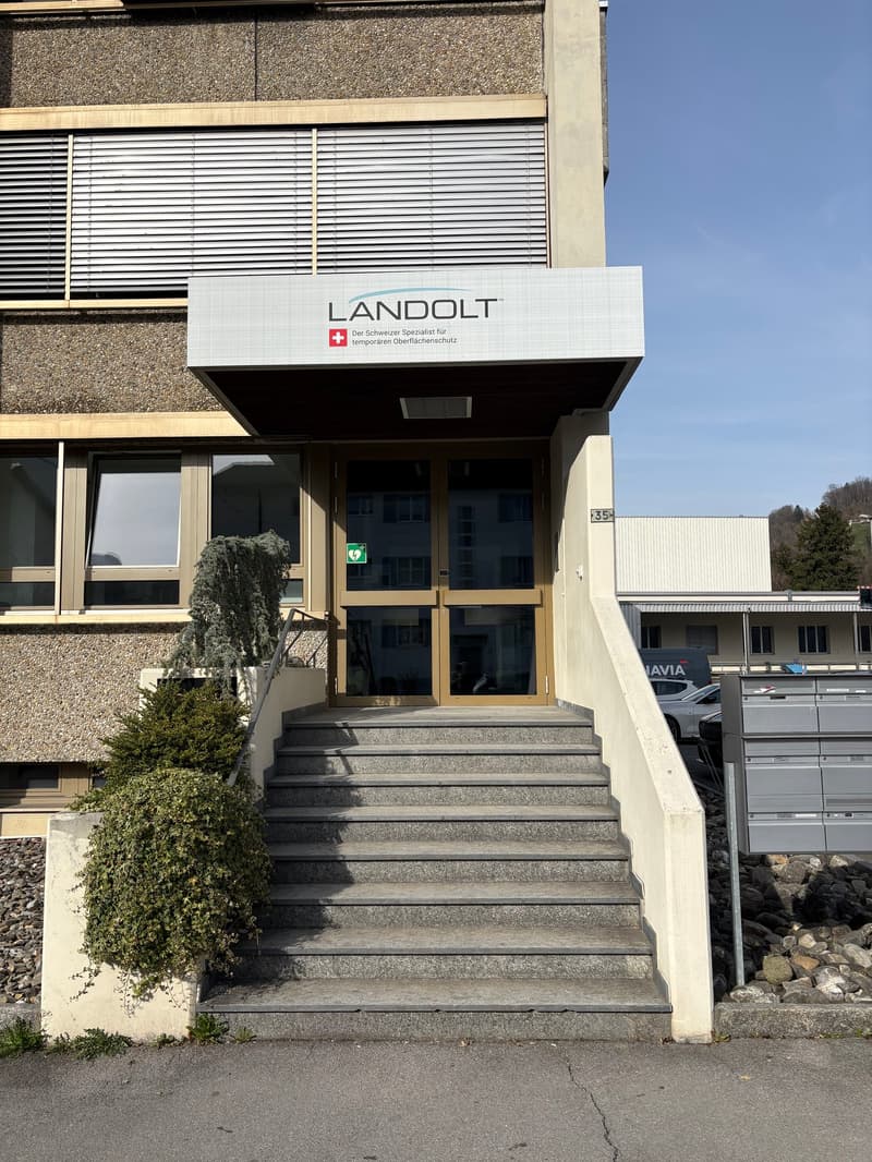 LANDOLT entrance with stairs, glass door, and signboard, concrete base, greenery.