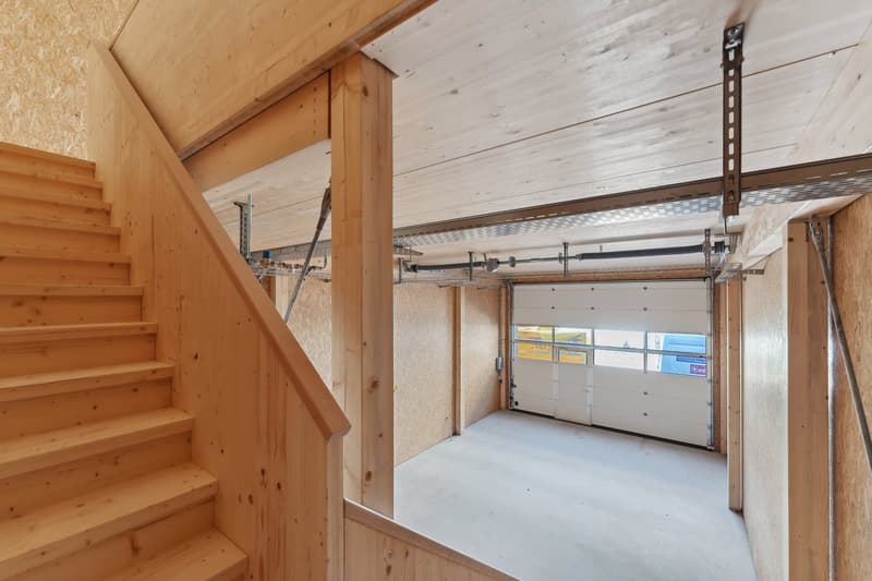 Garage with an open door, concrete floor, wooden ceiling, and wooden staircase