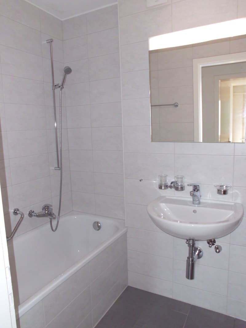 Modern bathroom with white tiles, bathtub, shower, sink, and mirror.