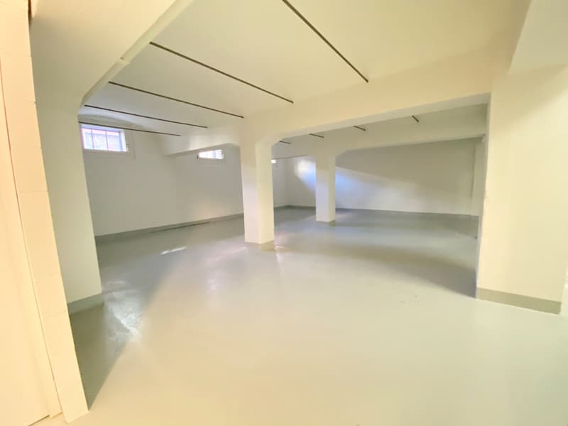 Large open space with high ceilings, white walls, and concrete flooring. The room appears to be an unfinished or renovated space, with exposed beams and windows providing natural light.