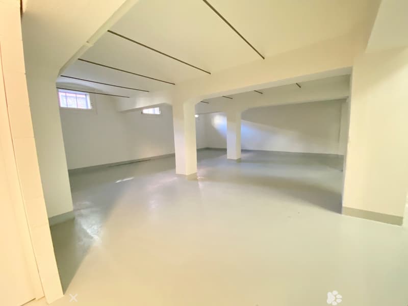 Large open space with high ceilings, white walls, and concrete flooring. The room appears to be an unfinished or renovated space, with exposed beams and windows providing natural light.
